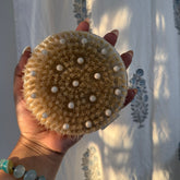 Hand holding a round, textured object with white dots against a light fabric background
