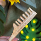 Wooden comb held by a hand with a sunflower and decorative leaves in the background